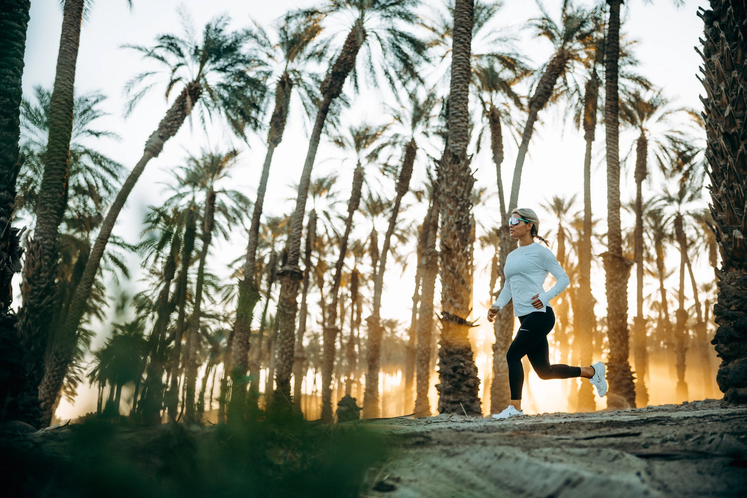 Kvinde løber mellem palmer med 100% solbriller